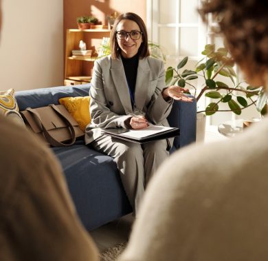 Young social worker in suit sitting on sofa in the living room and talking to foster parents about custody at meeting at home